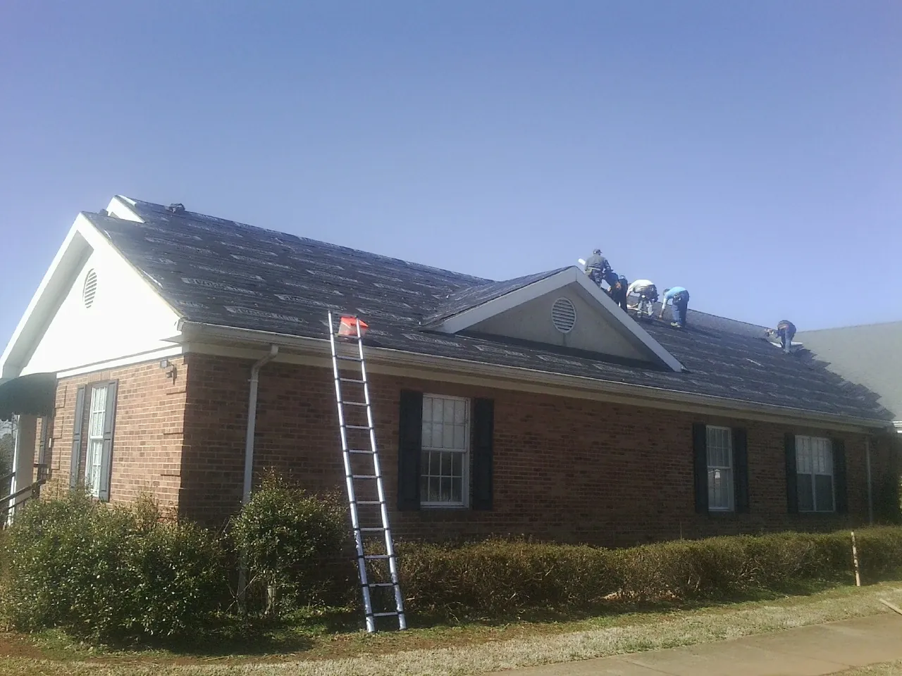 Crew tearing shingles off a brick ranch roof with a ladder set — Emergency Roof Repair work by our crew in Cheltenham