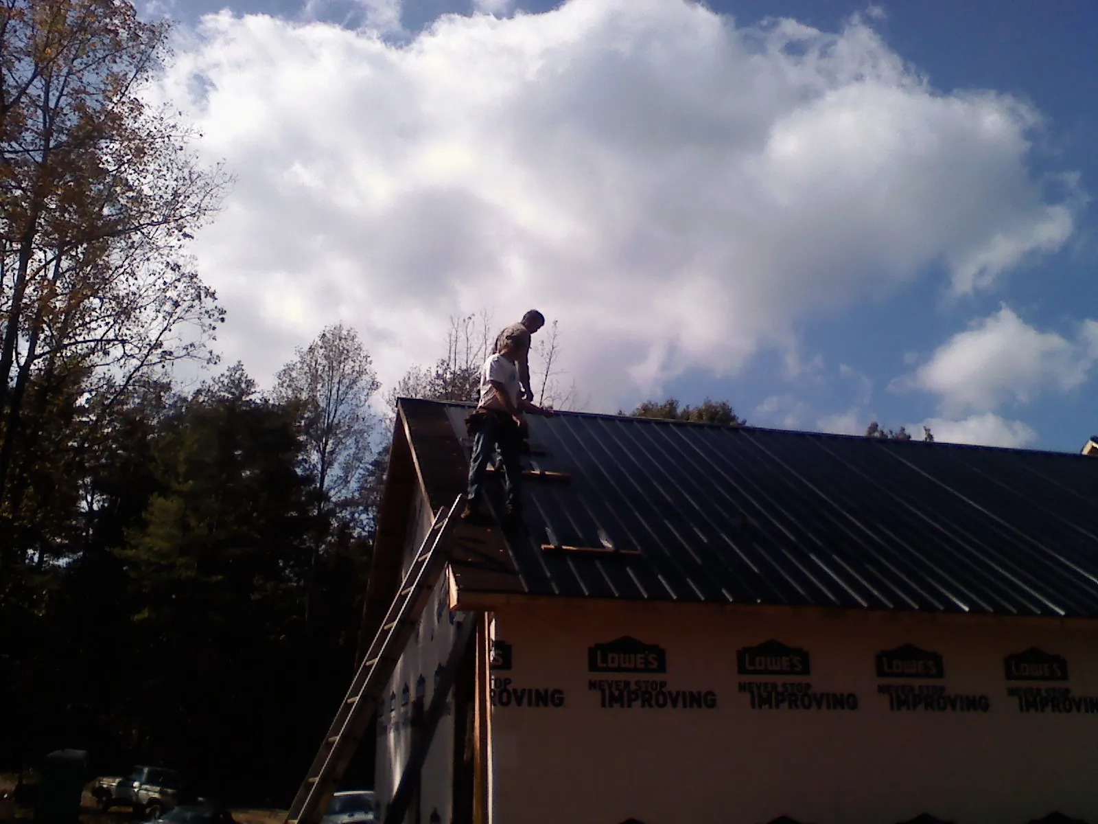Roofer fastening dark metal panels high against a cloudy sky, from a Roof Inspection job in Cheltenham