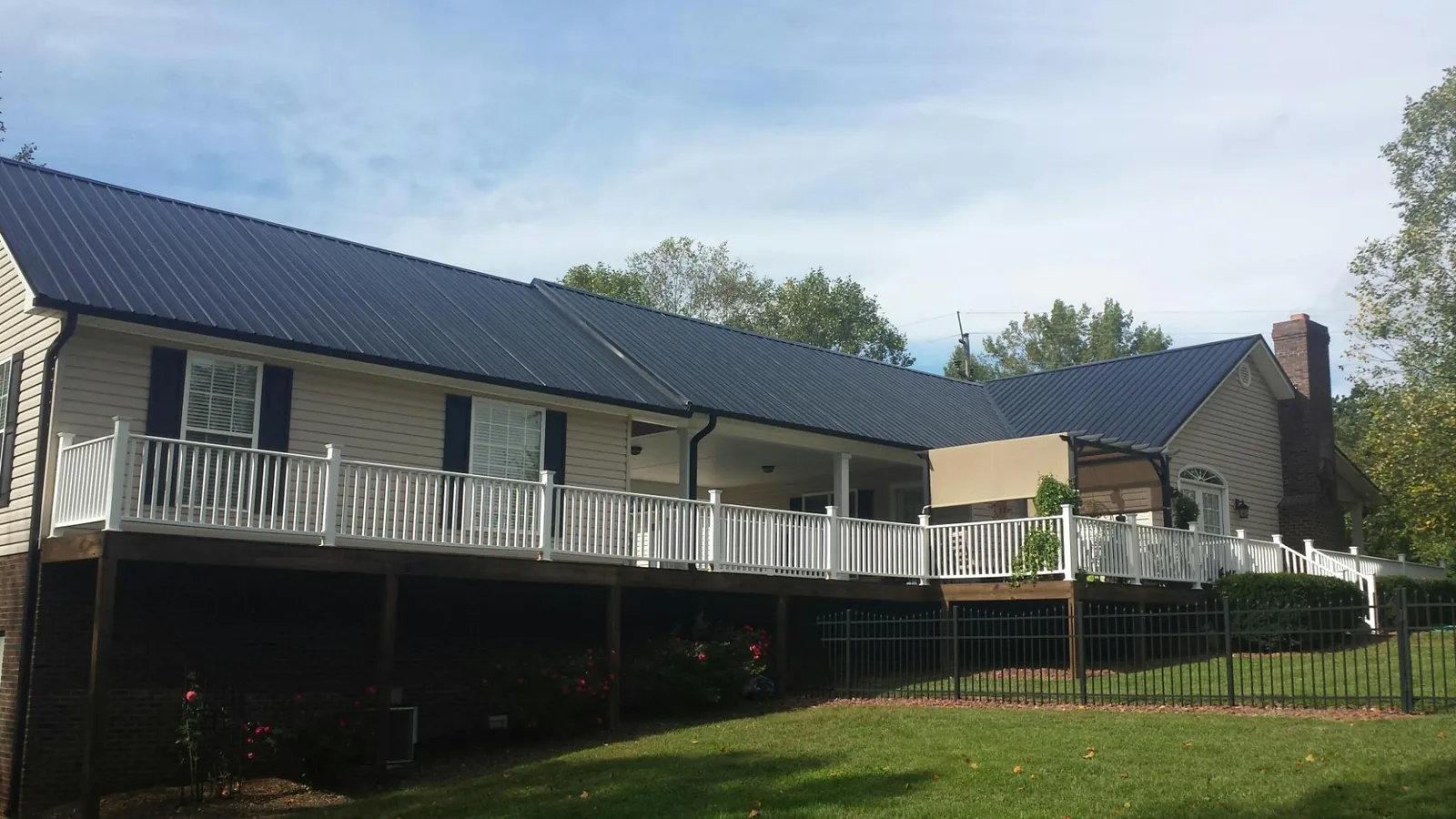 Black metal roof above a long white railed deck on a hillside home in Cheltenham
